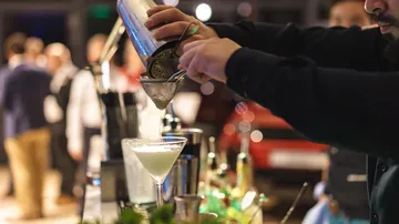 Barkeeper gießt Cocktail in Glas an Bar.