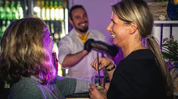 Two women laughing at a bar with bartender.