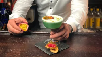 Bartender serves green cocktail with passion fruit.