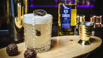 Cocktail with garnish on wooden board, bar background.
