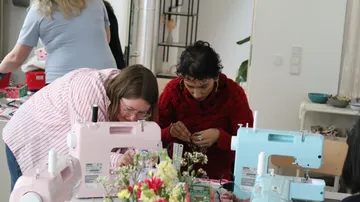 Menschen nähen an einem Tisch mit Maschinen.