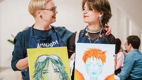 Two people hold painted portraits in an art class.