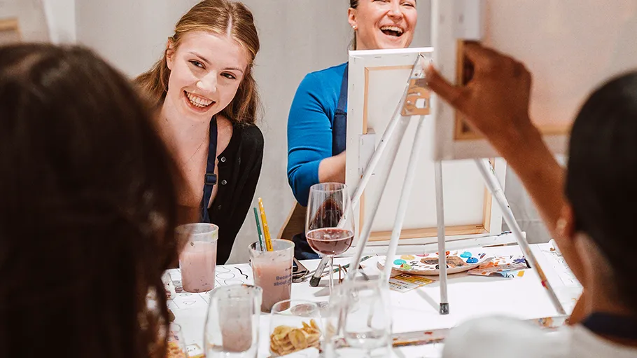 People laughing, painting at table together.