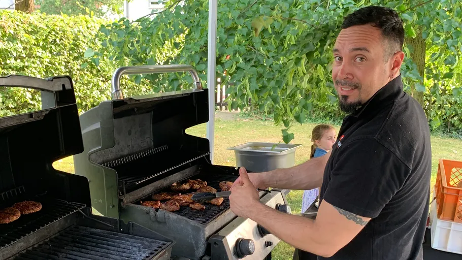 Mann grillt Burger im Freien unter Bäumen.