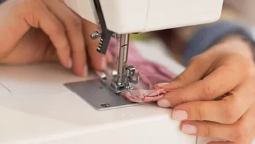 Eine Nähmaschine näht einen pinken Stoff in heimischer Umgebung.
