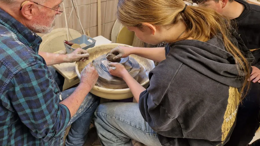 Person teaching pottery on a spinning wheel indoors.