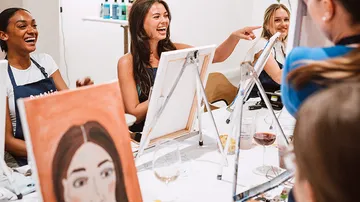 Women laughing and painting at a table.