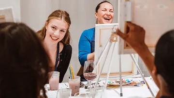 Frauen lachen und malen an einem Tisch.