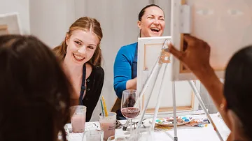 Women laughing and painting at a table.