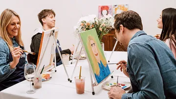 People painting at a table, smiling, enjoying art.