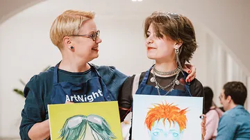 Two people holding paintings at art event.