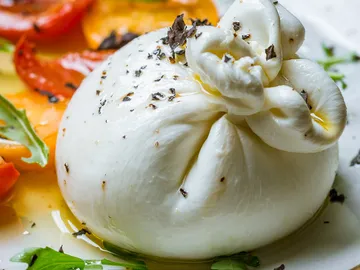 Burrata liegt auf einem Teller, umgeben von Gemüse.