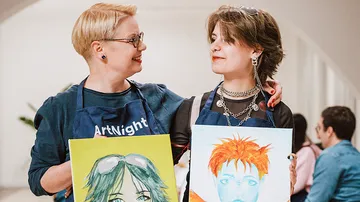 Zwei Personen halten Gemälde bei Kunstveranstaltung.