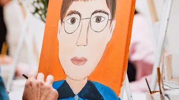 Person painting portrait on orange canvas.