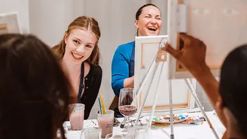 Women laughing at painting class with drinks.