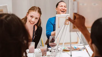 Frauen lachen bei einer Gruppenmalsektion.