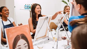 Frauen malen und lachen bei Veranstaltung.