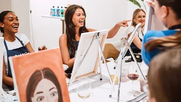 Women laughing and painting at a table.
