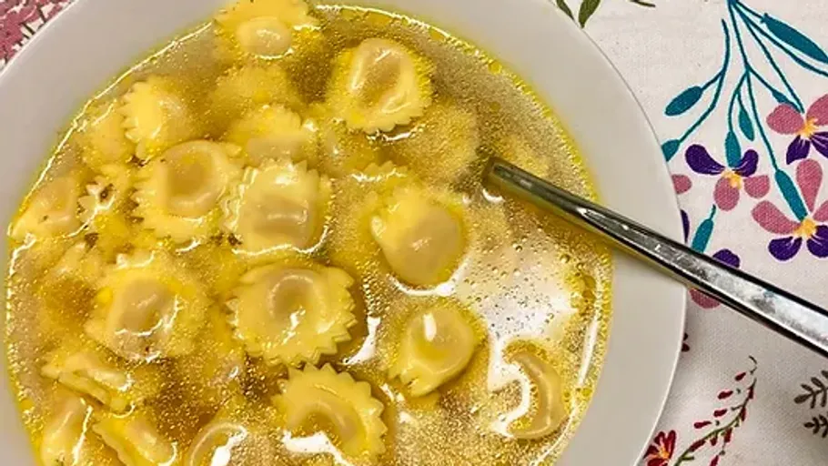 Ravioli in broth with a spoon, floral tablecloth.