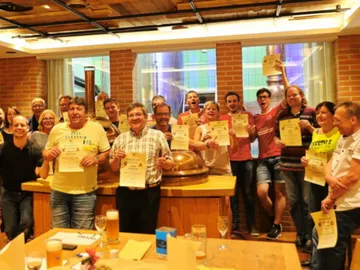 Gruppe von Menschen feiert mit Urkunden in Brauerei.