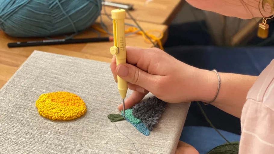 Person using punch needle on fabric canvas.