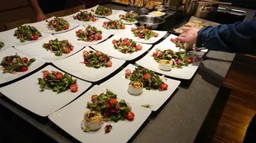Teller mit Salaten und Käse auf Arbeitsplatte.