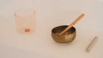 Singing bowl and glass cylinder on white surface.