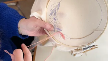 Person embroidering leaf design on fabric.