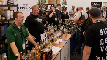 People tasting whiskey at a crowded festival.