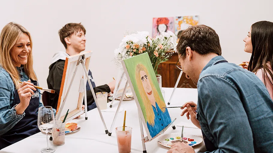 Group painting at easels, smiling, indoors.