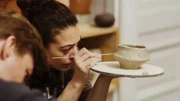 Person sculpting clay bowl with a stick.