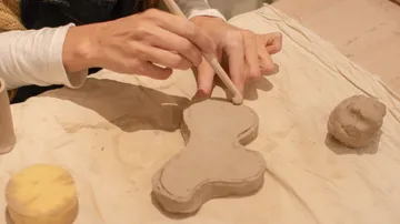 Hands shaping clay on a table.