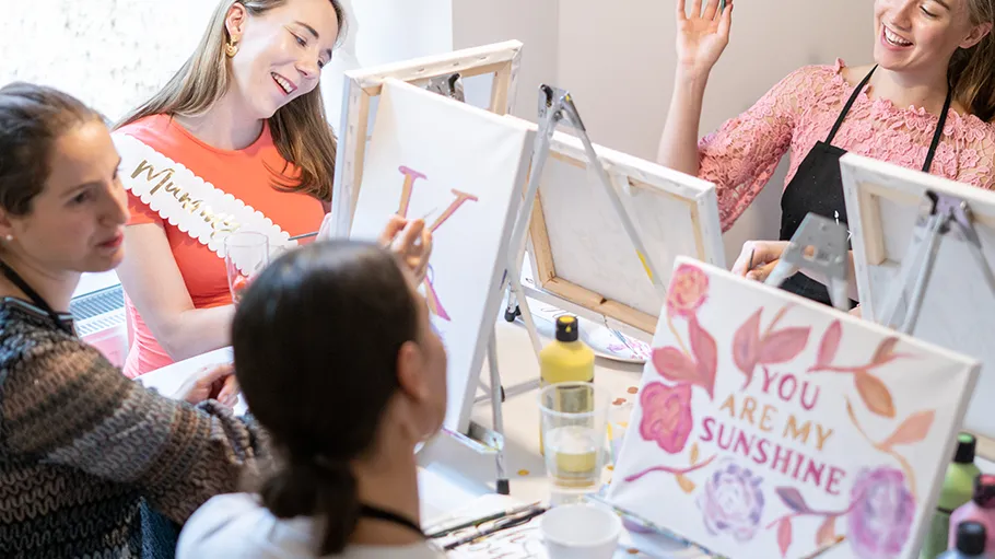 Women painting at easels, laughing together.