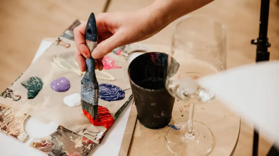 Hand painting with brush near wine glass.