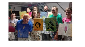 Group of people holding paintings indoors.