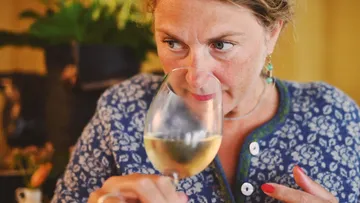 Woman sniffing wine glass indoors.