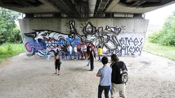 People viewing graffiti under a bridge.