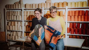 Two people holding colorful fabric pieces in workshop.