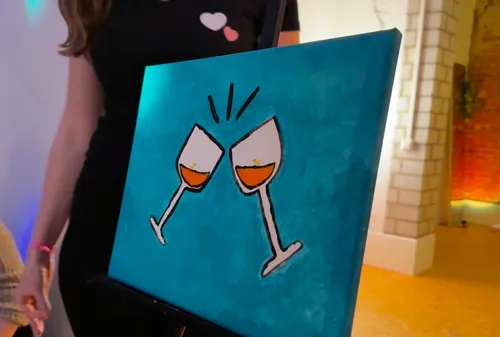 Woman holding canvas with clinking glasses painting.