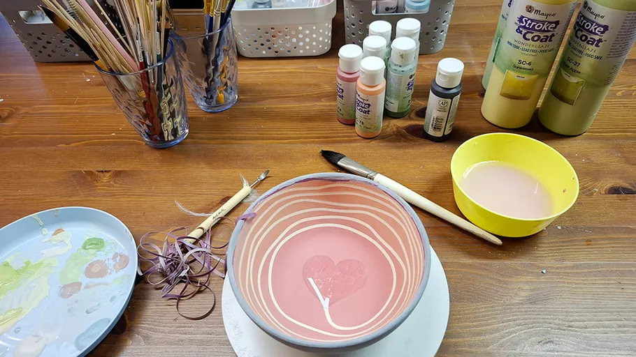 Painted bowl with brushes and paint bottles.