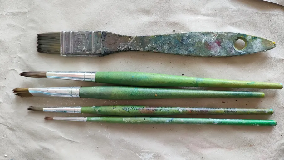 Five paintbrushes lying on paper.