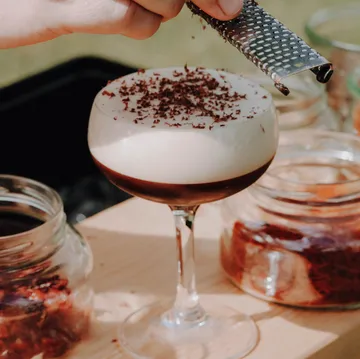 Hand grating chocolate over a creamy cocktail.