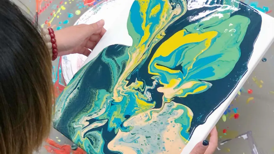 Person tilting canvas with colorful fluid art.