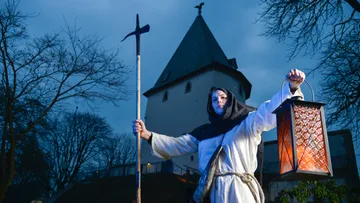 Person in historischer Kleidung hält Laterne draußen.