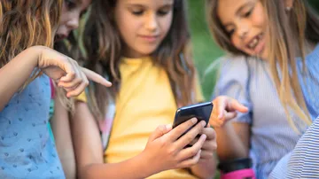 Three girls looking at smartphone outdoors.