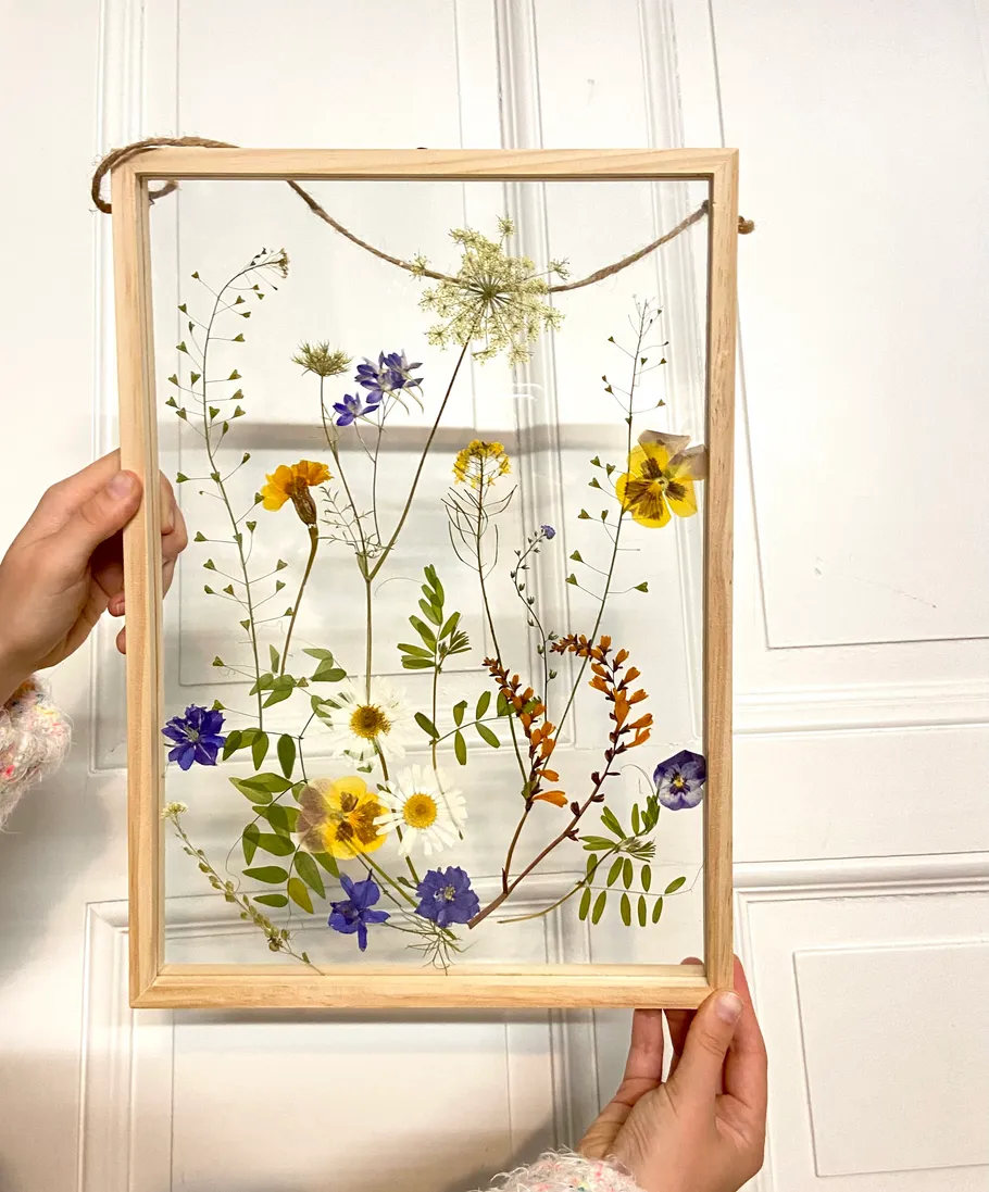 Pressed flowers in wooden frame held by hands.