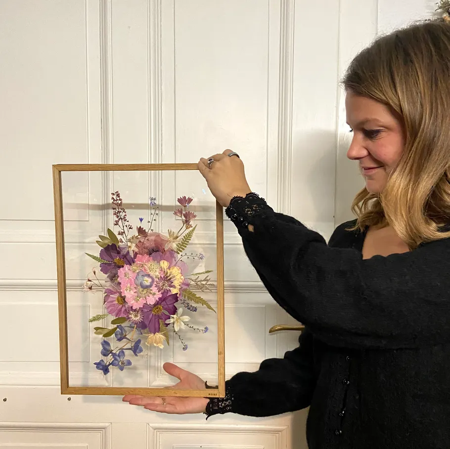Woman holding floral artwork in frame.