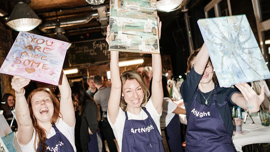 Three women holding up their paintings indoors.