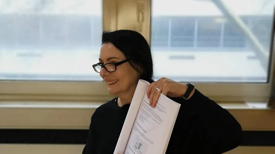 Frau hält Dokumente, lächelt drinnen.