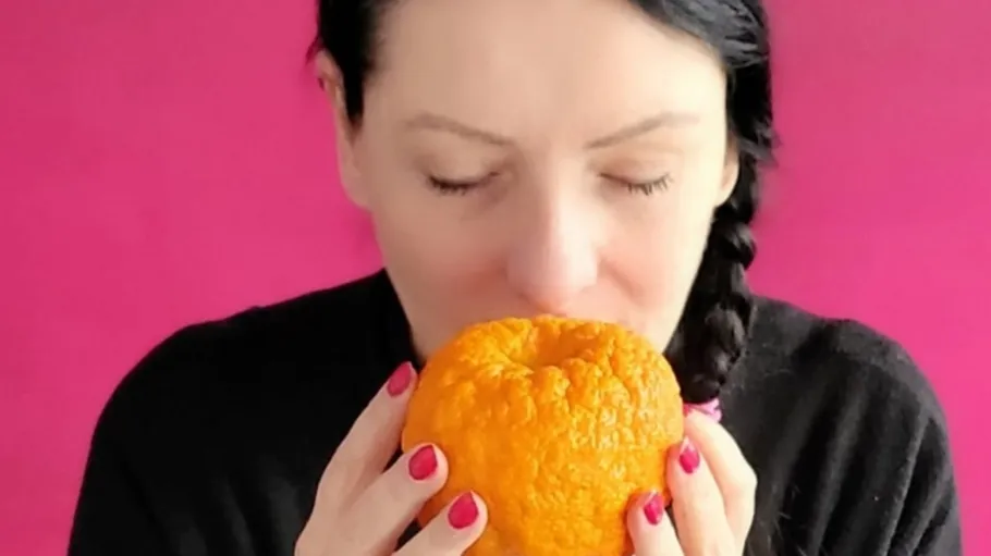 Woman smelling large orange fruit indoors.